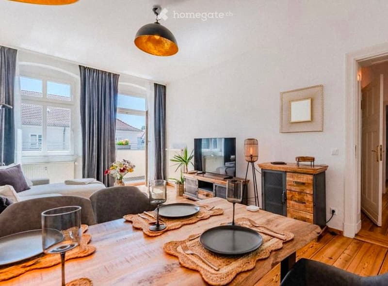 A modern, well-lit living and dining area with a sofa, dining table with chairs, television, decorative lamp, mirror, and potted plants. The space features large windows with curtains and a warm, inviting atmosphere.