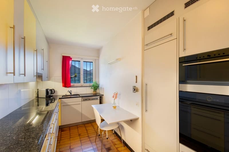 Modern kitchen with white cabinets, granite countertop, stainless steel appliances, and a small dining area with a table and chair.