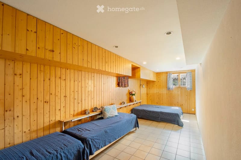 Cozy bedroom with wooden walls, two single beds, built-in shelves, and a small window with curtains.