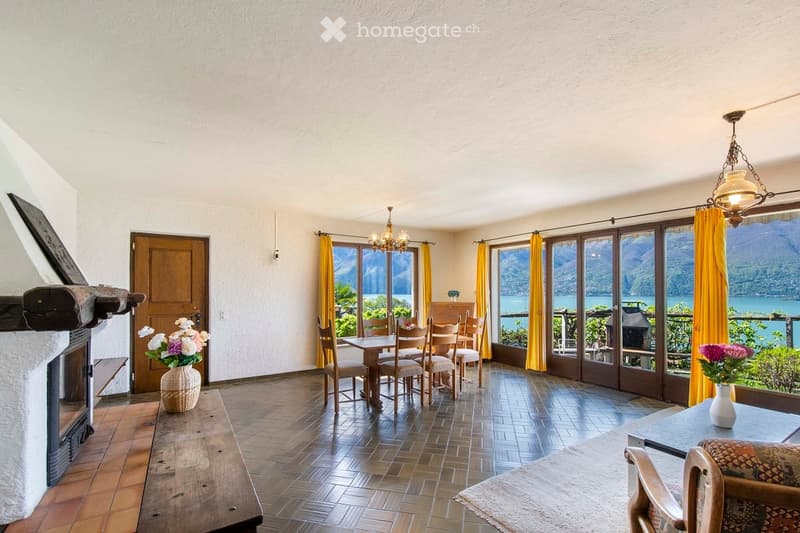 Bright dining area with wooden flooring, large windows offering scenic views, a dining table with chairs, a fireplace, and decorative vases.