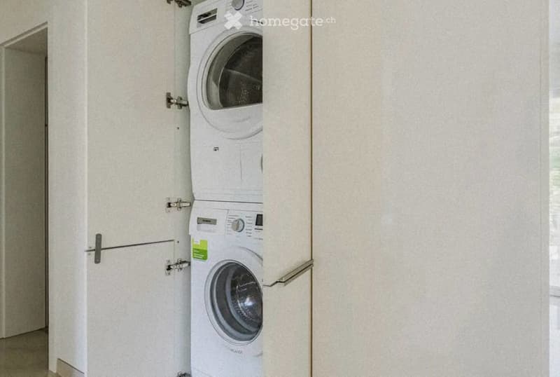 A compact, modern bathroom with a stacked washer and dryer unit, white walls, and a tiled floor.
