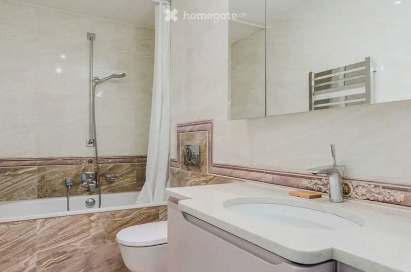 Modern bathroom with a bathtub, toilet, sink, and mirror. Features a marble accent wall and a sleek chrome showerhead.