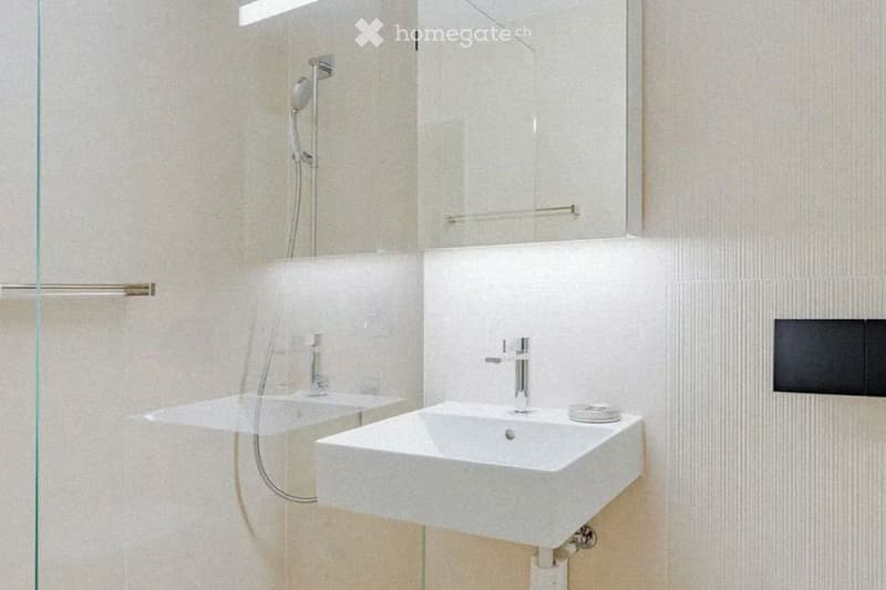 Modern bathroom with a white sink, a large mirror, and a glass shower enclosure. The walls are tiled in a light beige color, and the fixtures are sleek and contemporary.