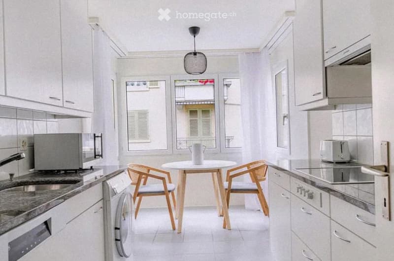 Modern kitchen with white cabinets, granite countertops, and stainless steel appliances. Includes a small dining area with a round table and two chairs.