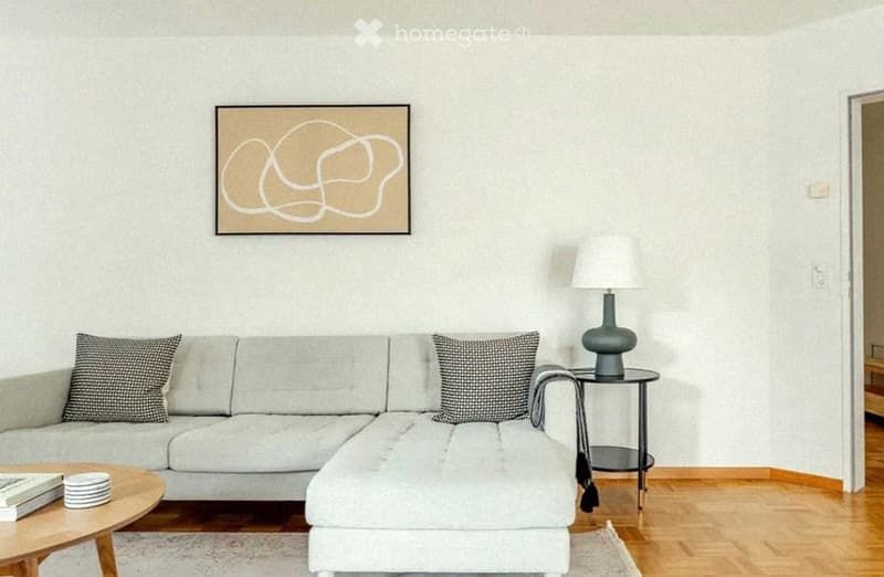 Modern living room with a grey sectional sofa, wooden coffee table, side table with a floor lamp, and a decorative picture frame on the wall.