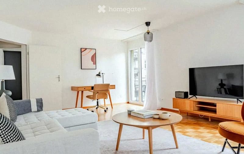 A modern living room with a white sofa, coffee table, TV, desk, and a large window with a view.