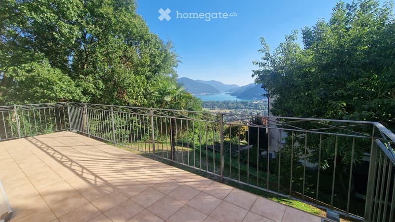Balcony with metal railing, tiled floor, overlooking a scenic lake and mountains.