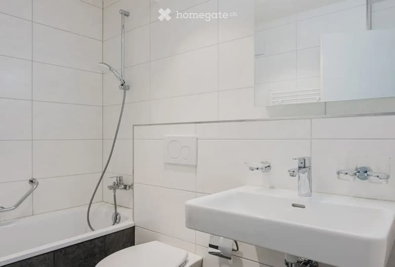 Modern bathroom with white tiles, a bathtub, toilet, sink, and a mirror above the sink.