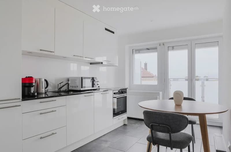 Modern kitchen with white cabinets, stainless steel appliances, and a small dining area with a round table and chairs.