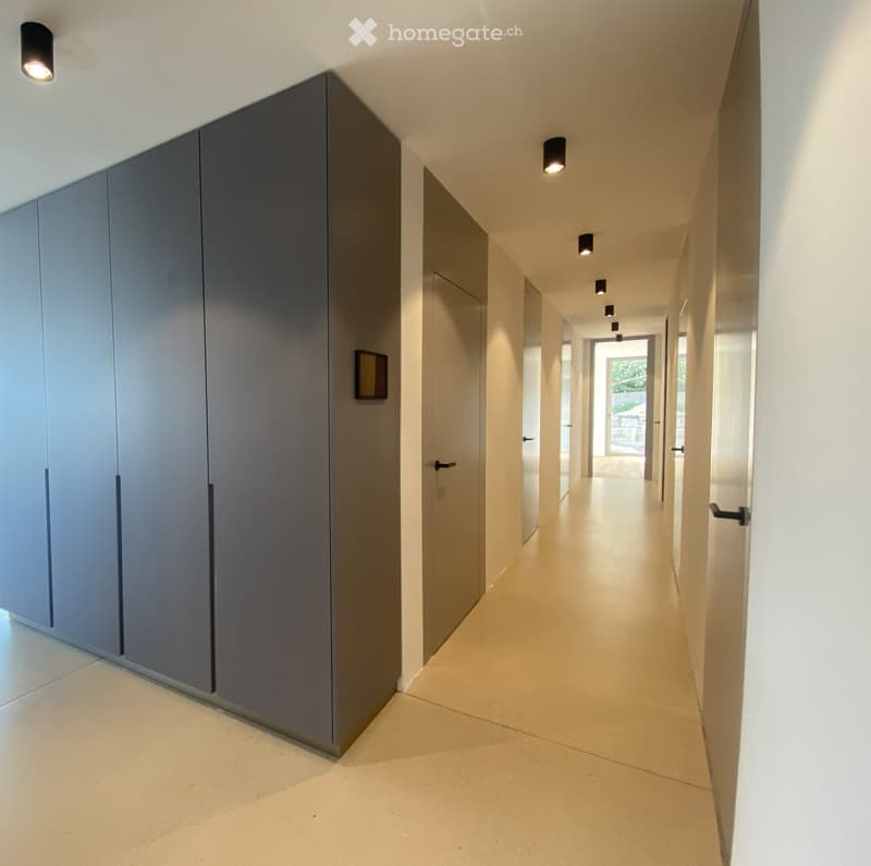 Modern hallway with light-colored walls, recessed lighting, and grey cabinetry on one side.