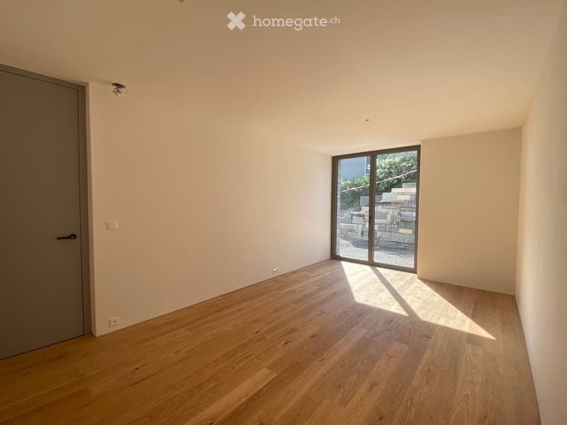 Empty room with light-colored wooden flooring, white walls, and a large sliding glass door leading to an outdoor area.