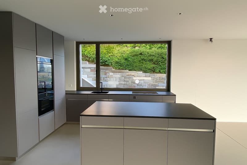 Modern kitchen with grey cabinets, a central island, and a large window overlooking a garden.