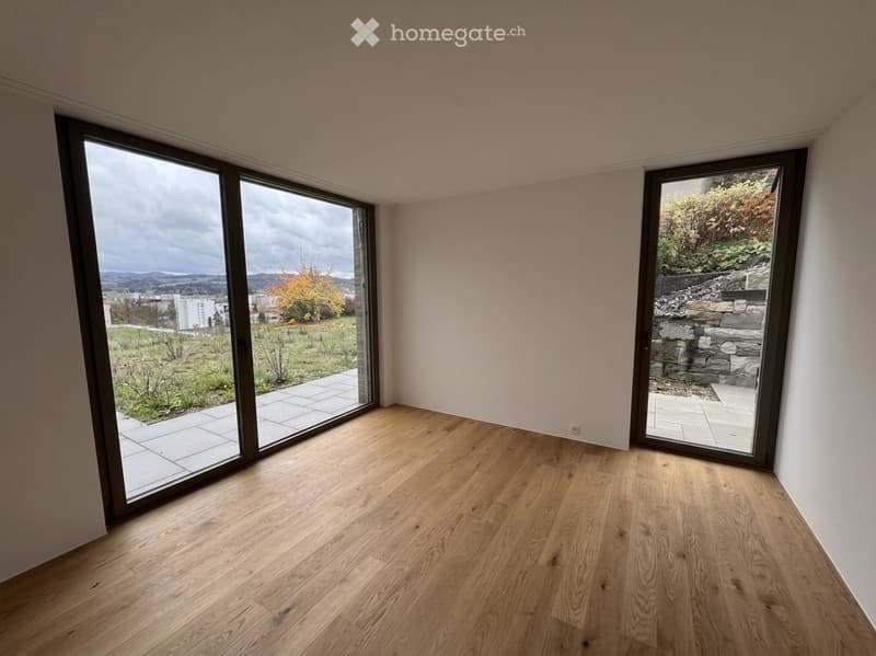 Empty room with wooden flooring and large sliding glass doors leading to a patio and outdoor area.