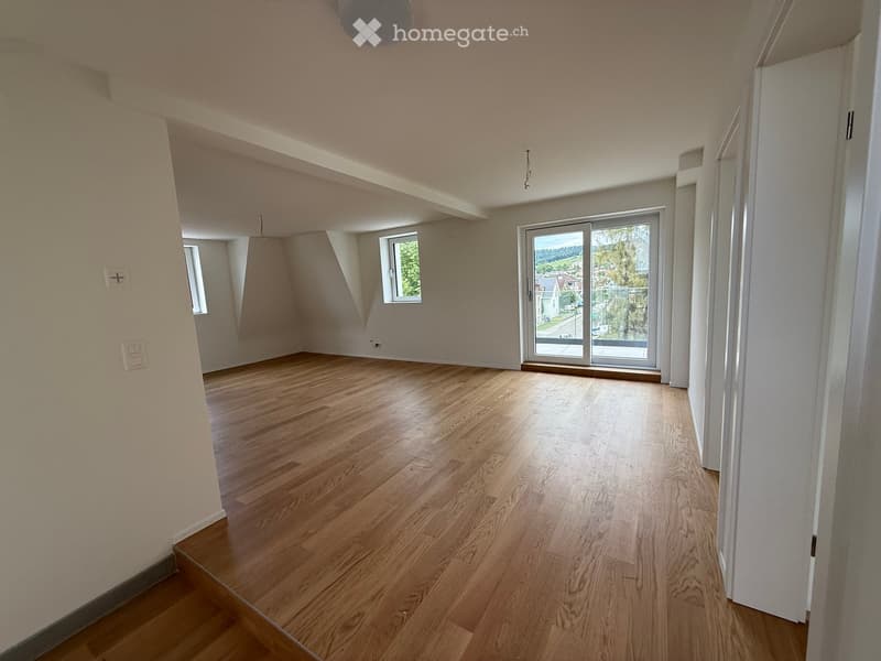 Empty room with wooden flooring, white walls, and large windows, including a sliding glass door leading to a balcony.