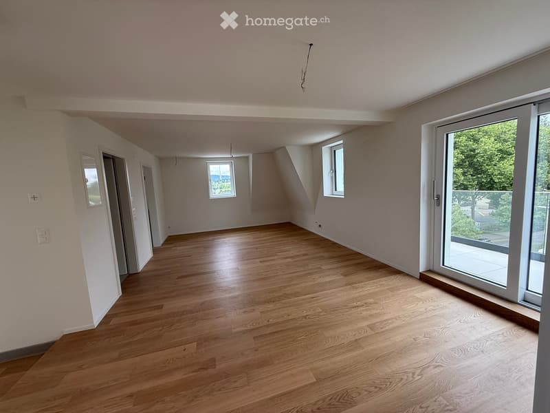 Empty room with wooden flooring, white walls, and large windows, including a sliding glass door leading to a balcony.