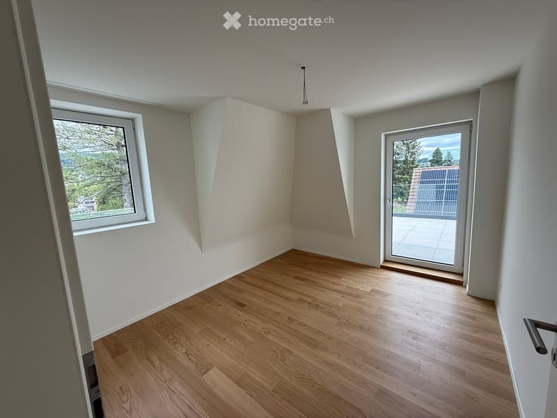 Empty room with wooden flooring, white walls, large windows, and a sliding glass door leading to a balcony.