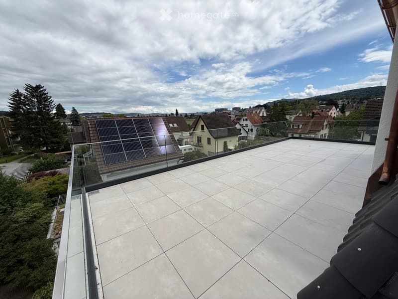 Roof terrace with tiled floor, glass railing, and scenic view of neighborhood houses and solar panels on a nearby roof.