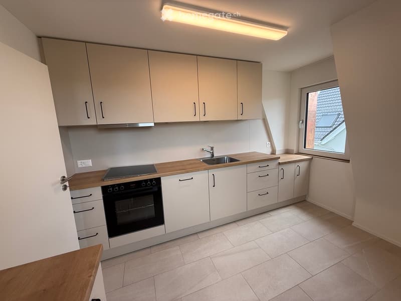 Modern kitchen with white cabinets, wooden countertops, built-in oven, sink, and a window overlooking a roof.