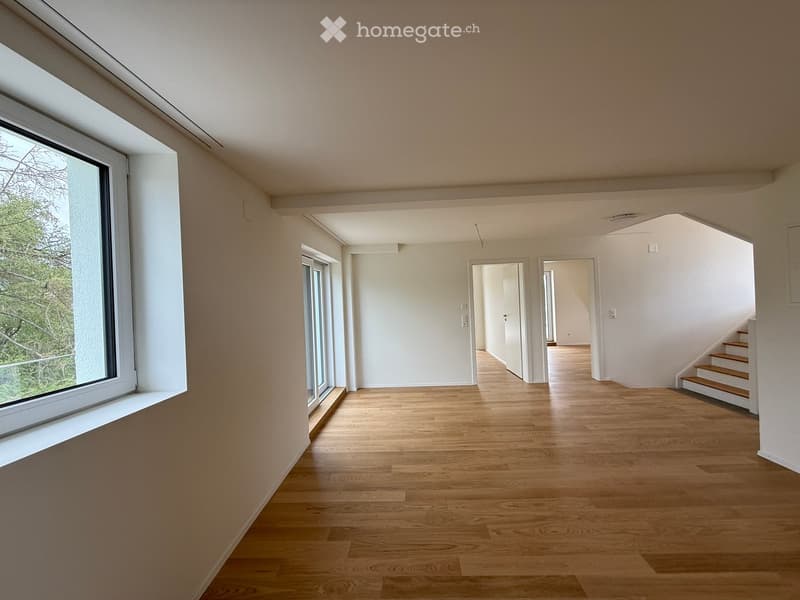 Empty hallway with wooden flooring, white walls, large windows, and doors leading to other rooms.