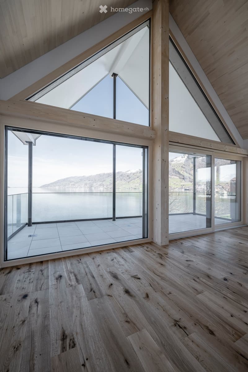 Bright, airy attic space with wooden floors, large skylights, and expansive windows overlooking a lake and mountains.
