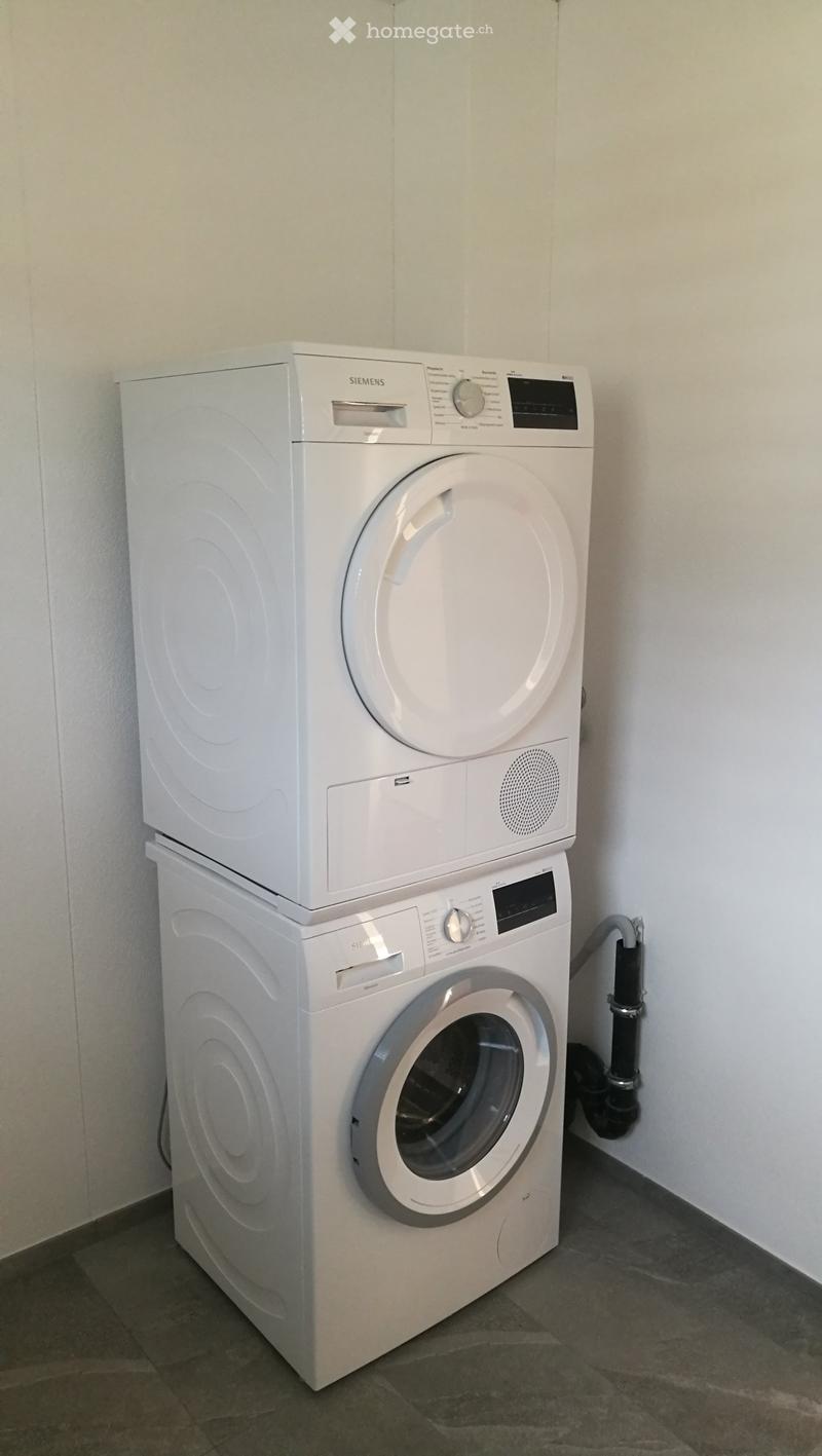 A compact bathroom with a stacked washing machine and dryer unit, featuring a sleek white design and modern control panels.