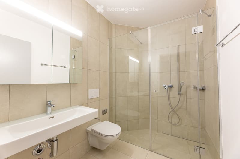Modern bathroom with white tiles, glass shower enclosure, silver faucet, white toilet, built-in mirror