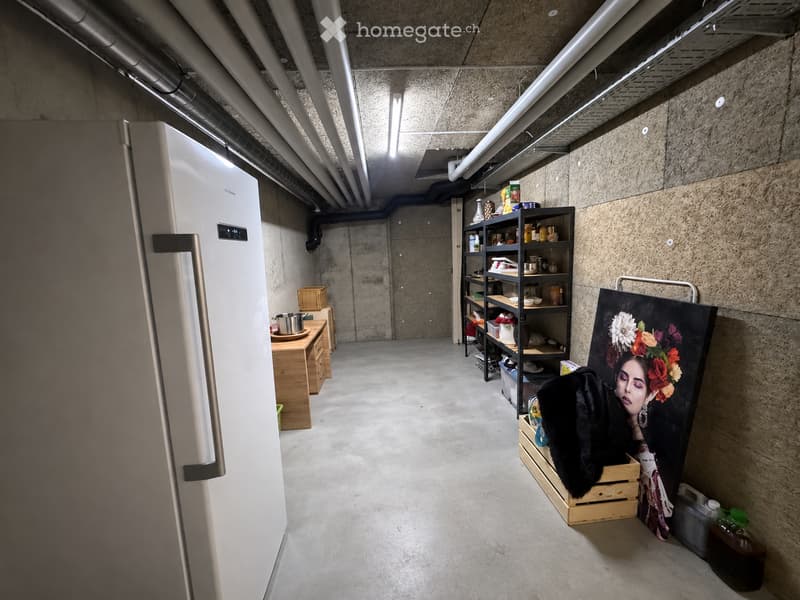 A modern, industrial-style kitchen with a stainless steel refrigerator, wooden shelves, a small table, and a large painting leaning against the wall.