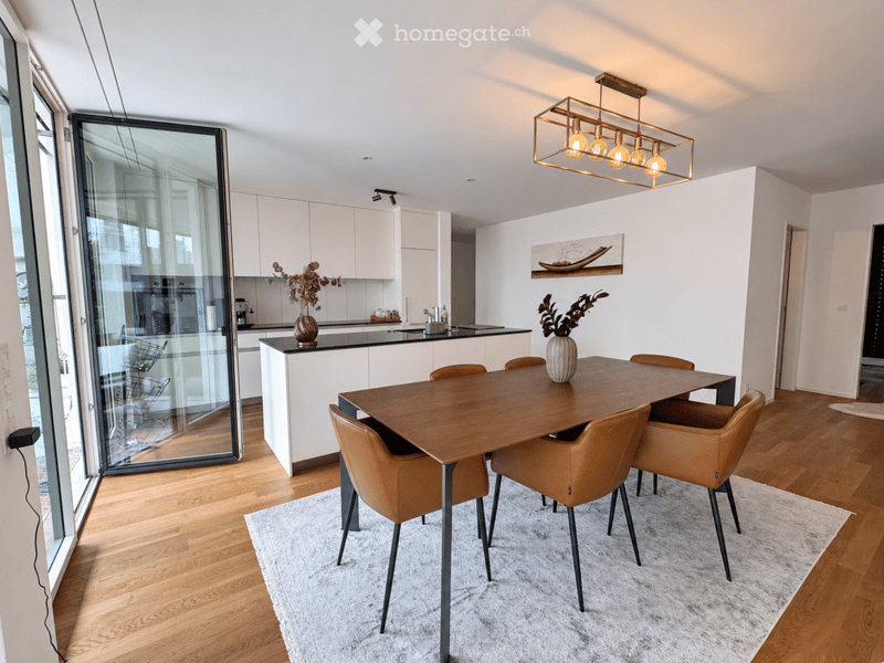 Modern dining area with a wooden dining table, brown leather chairs, a white rug, and a sleek kitchen area with white cabinets and a black countertop.