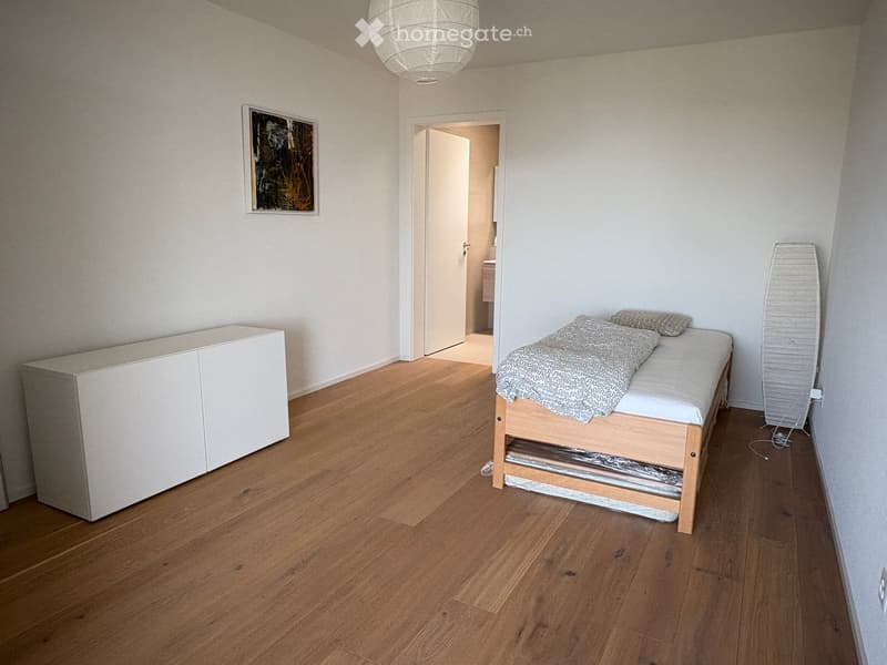 Minimalist bedroom with wooden flooring, a single bed with a blanket, a white cabinet, and a picture frame on the wall.