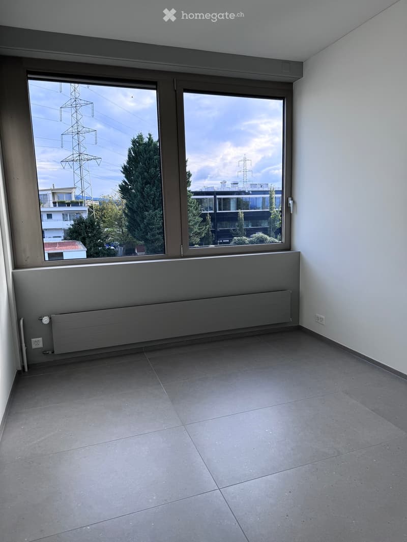 Empty room with large windows, tiled floor, radiator, and visible electrical outlets.