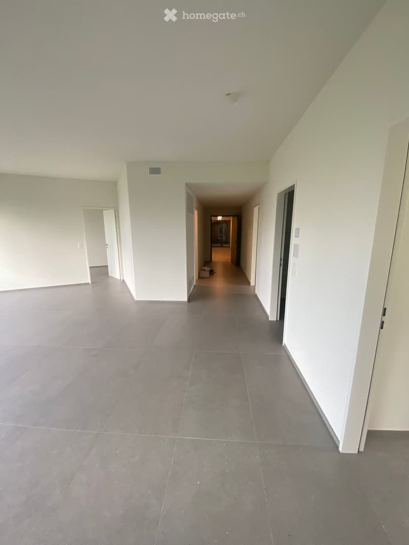 Empty hallway with grey tiled floor, white walls, and several doors leading to other rooms.
