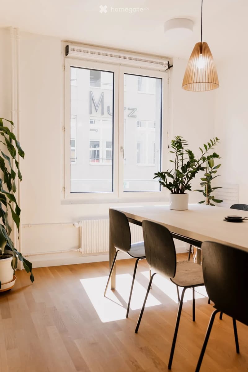 Bright dining area with a white table, four chairs, and potted plants near large windows.