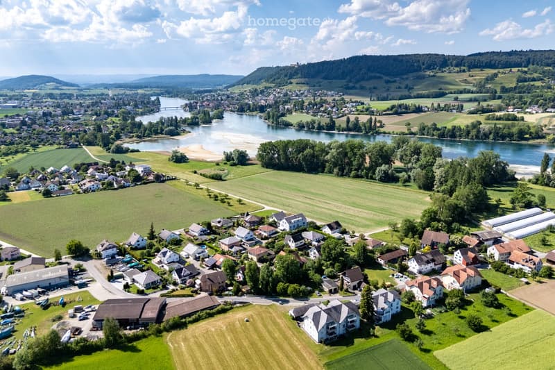 Aerial view of a small village with houses, fields, and a river running through it.
