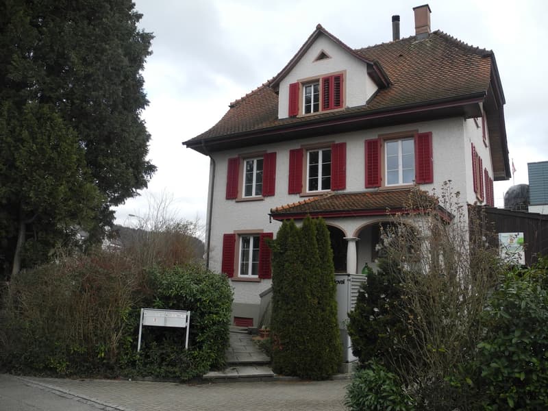 Two-story house with white exterior, red shutters, tiled roof, and a small porch area with steps leading to the entrance.