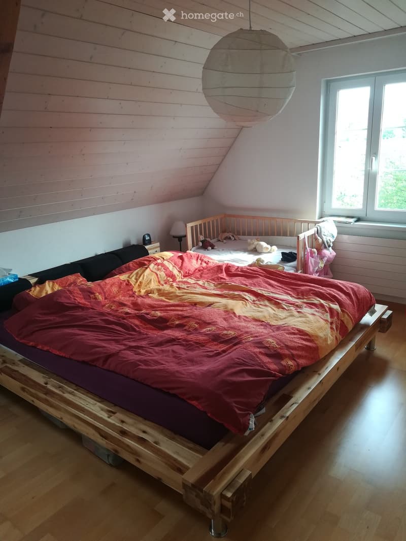 Cozy bedroom with wooden bed frame, red and yellow duvet, bedside table with lamp, and toys on the bed.