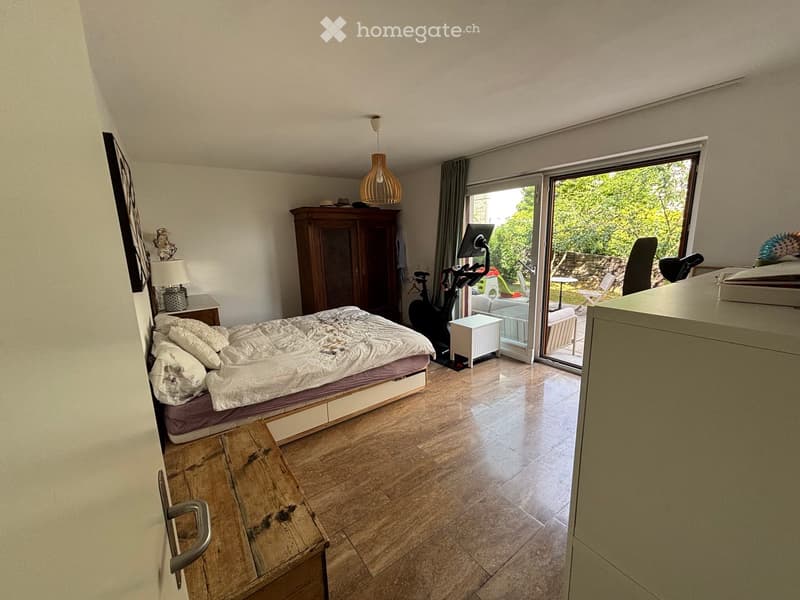 Bright bedroom with a large bed, wardrobe, exercise bike, and a sliding glass door leading to a garden.