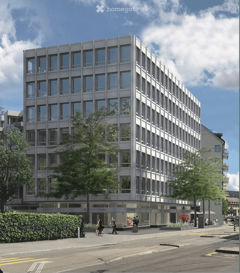 Modern multi-story building with large windows and a flat facade, surrounded by trees and a paved street with pedestrians.