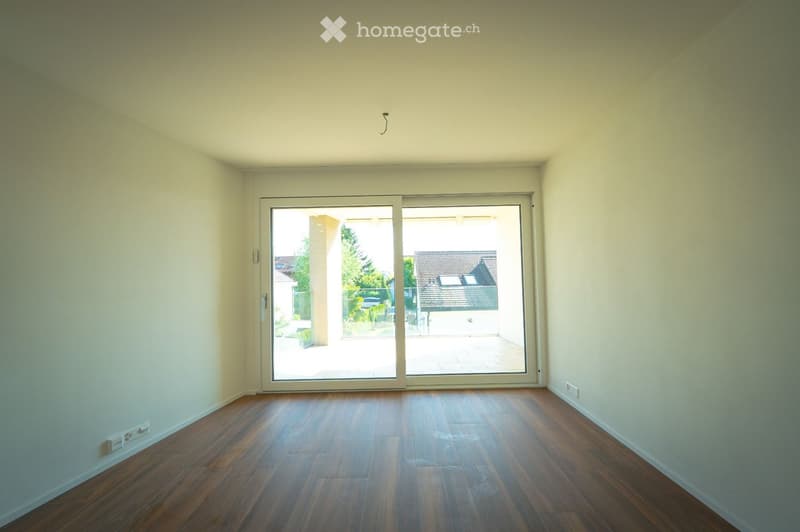 Empty room with wooden flooring, white walls, and large sliding glass doors leading to an outdoor area.