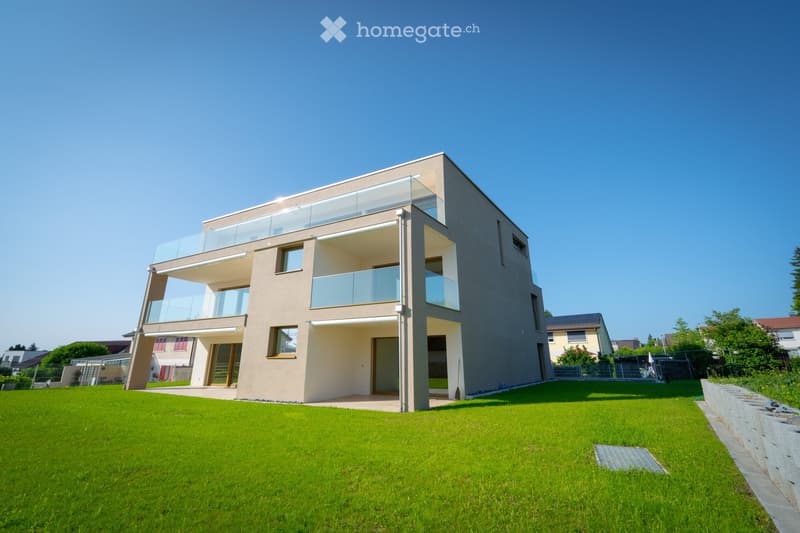 Modern two-story house with large windows and balconies, surrounded by a well-maintained lawn.