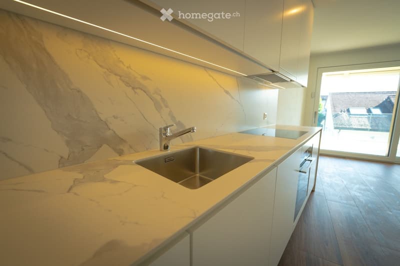 Modern kitchen with marble countertop, stainless steel sink, and sleek white cabinets.