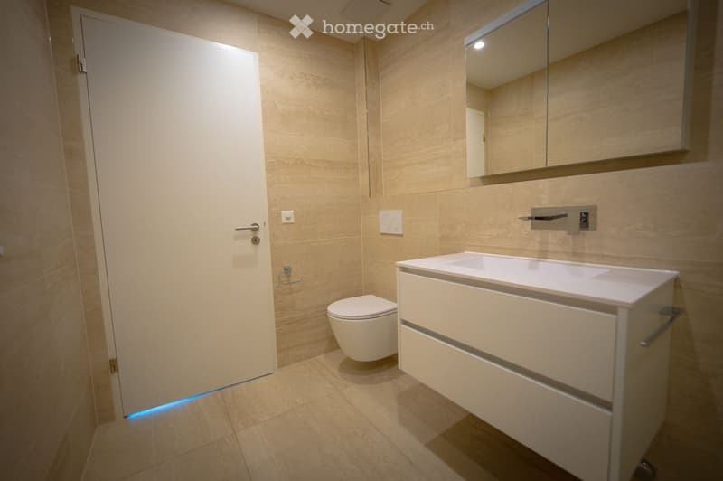 Modern bathroom with beige tiles, a white sink with a cabinet, a toilet, and a large mirror above the sink.