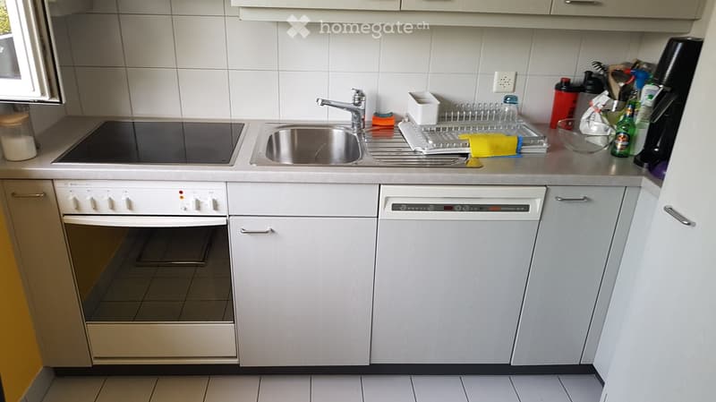 Modern kitchen with white cabinets, stainless steel sink, oven, dishwasher, and various kitchen items on the counter.