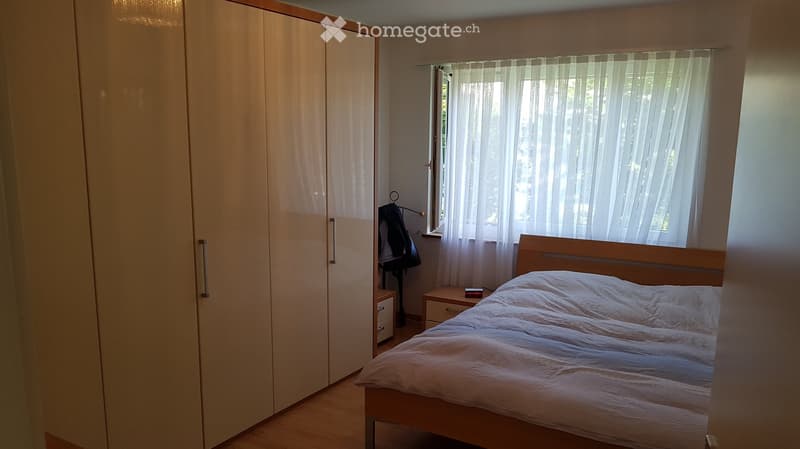Bedroom with a wooden bed, white bedding, a large wardrobe, a nightstand, and sheer curtains on the windows.