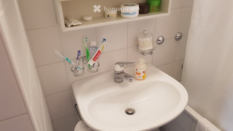 A modern bathroom sink with a chrome faucet, toothbrush holder, toothpaste tube, cotton swab holder, soap dispenser, and a shelf with various toiletries.