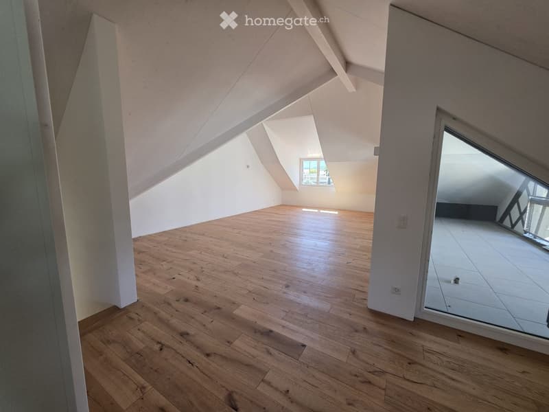 Empty attic room with wooden flooring, white walls, and skylight windows allowing natural light.
