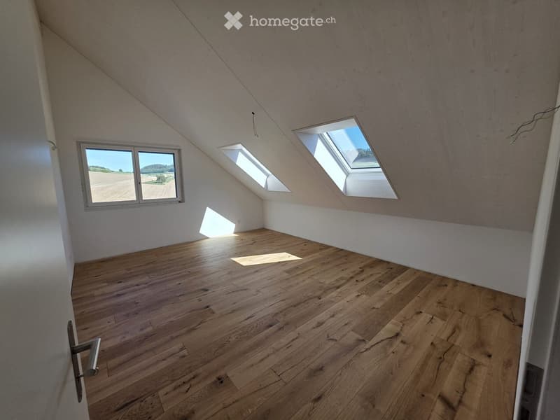 Empty attic room with wooden flooring, white walls, and skylight windows allowing natural light to enter.