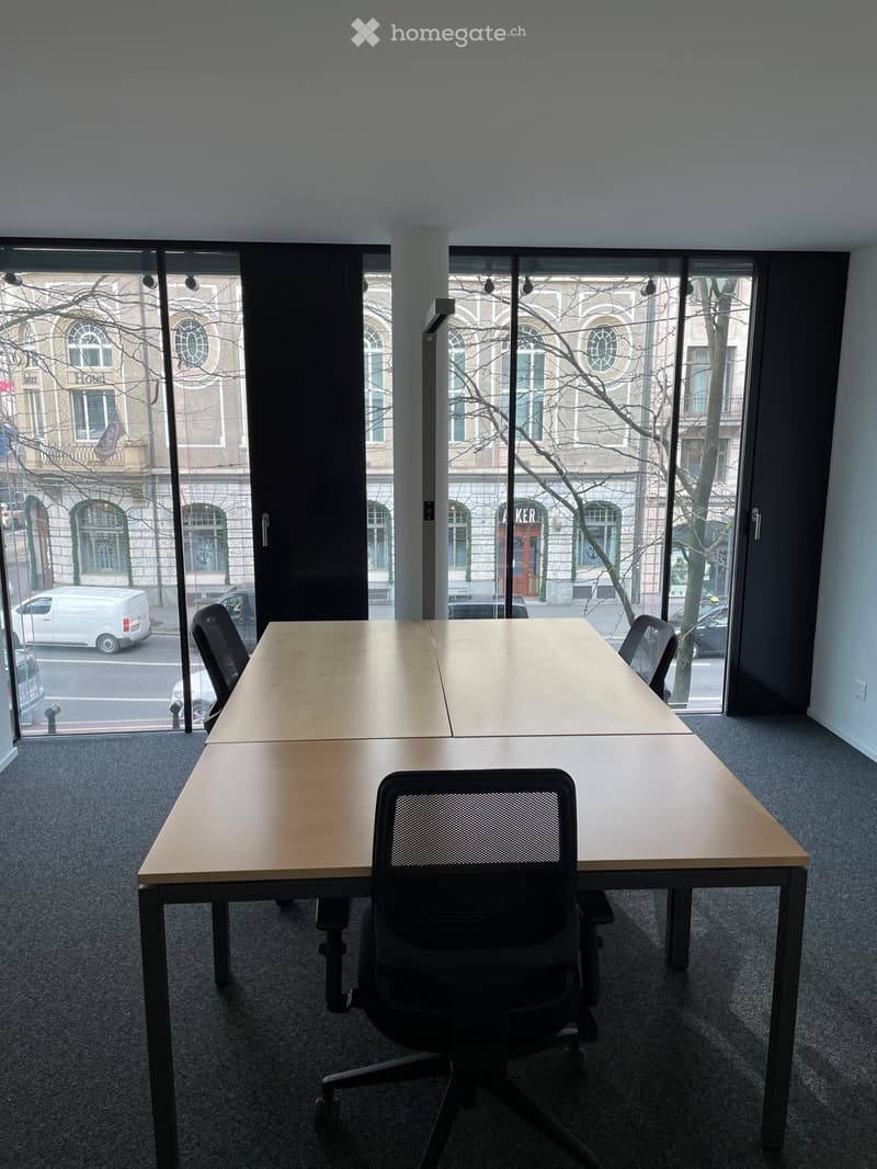 Office room with large windows, glass doors, long wooden tables, black chairs, carpeted floor