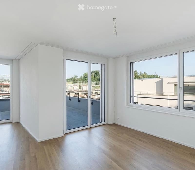 Empty room with wooden flooring, white walls, large windows, and a sliding glass door leading to a balcony.