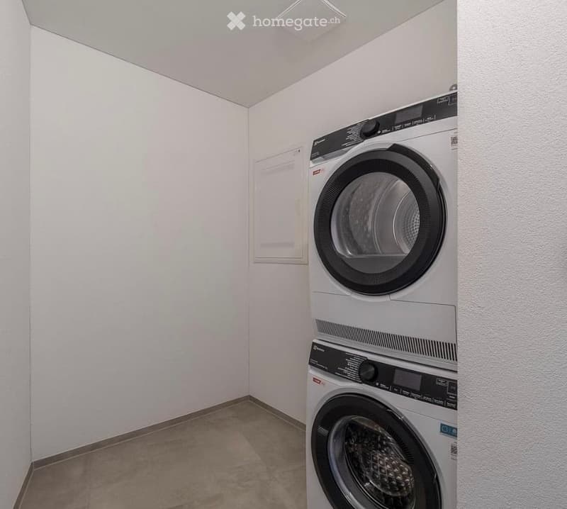 A small, clean bathroom with a stacked washer and dryer unit against the wall, white tiled walls, and a neutral-colored floor.