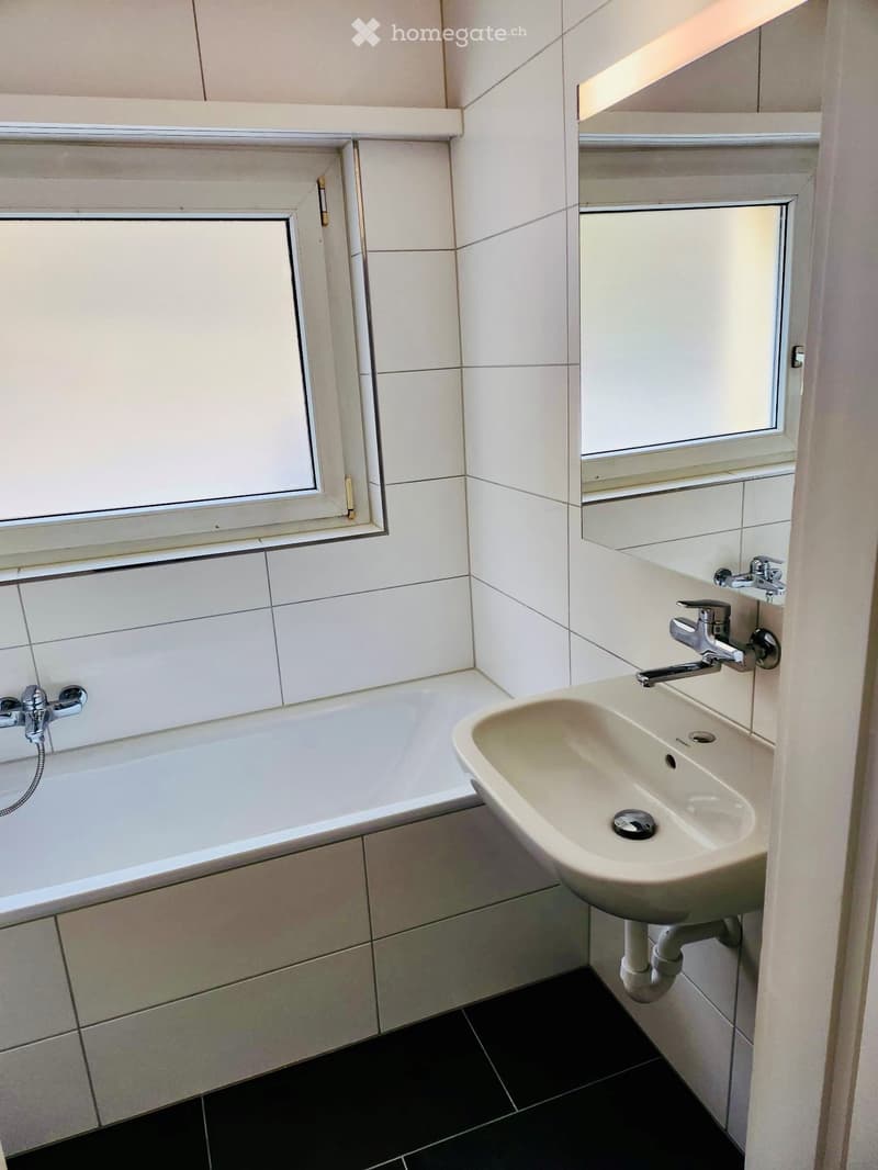 Modern bathroom with a bathtub, sink, and tiled walls. Features a window and sleek fixtures.